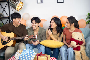 Singing. Man playing guitar at home with his friends at a party.group of young asian female and thai male happy smiling and sing a song with friends in birthday party at home