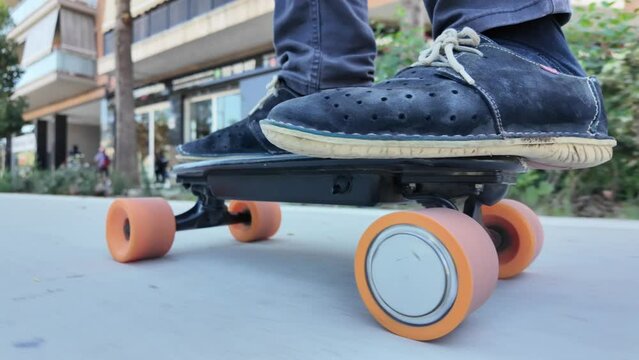 Person riding a small electric longboard through the city, focusing on wheels and feet. Urban sustainable and eco-friendly mobility. Zero emissions