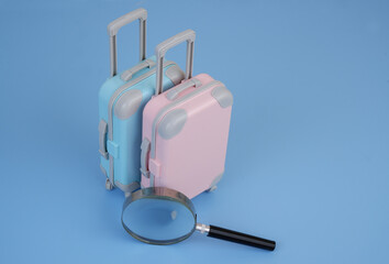 Checking travel baggage concept. Magnifying glass and two suitcases on blue background.