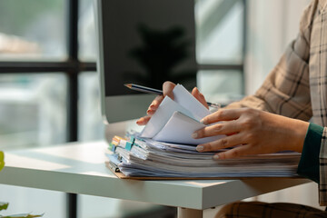 a secretary is organizing stack of paperwork for keep her desk clean, tidy up all finance document on desk because its so messy, a employee archive paper report for neat