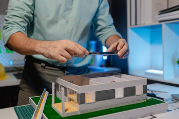 an engineer is doing a big project in the office, an architect uses electronic device to make the work he is doing easier, blueprint and model are on the desk, employee is working with concentration