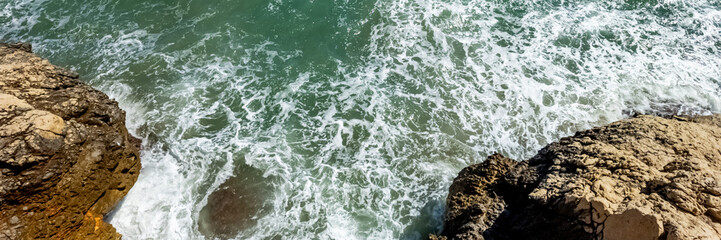 Aerial view of turbulent sea waves meeting rocky shore, ideal for travel themes, nature backgrounds, and World Oceans Day content