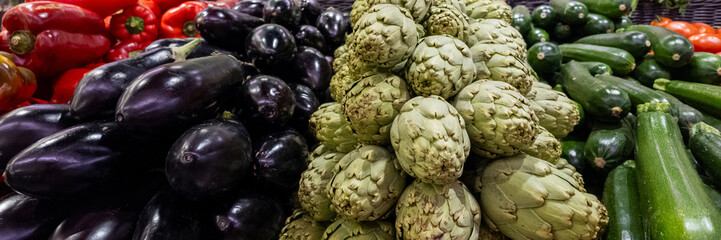 Fototapeta premium Assorted fresh vegetables display with artichokes, eggplants, red peppers, and zucchinis, ideal for culinary concepts and healthy eating themes