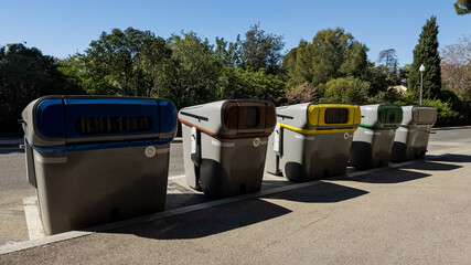 Row of color-coded recycling bins for waste segregation in a sunny outdoor setting, representing...