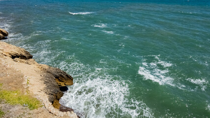 Sunny coastal scenery with waves crashing against rocks, ideal for summer vacation and World Oceans Day-related themes