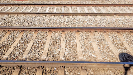 Parallel railroad tracks with textured gravel beds under bright daylight, ideal for concepts like travel, transportation, and industrial infrastructure