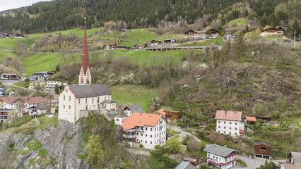 Aerial drone view of Oetz village during early springtime. Famous church standing on a rock in the Austrian village Oetz in Ötztal valley. Mountains in the background