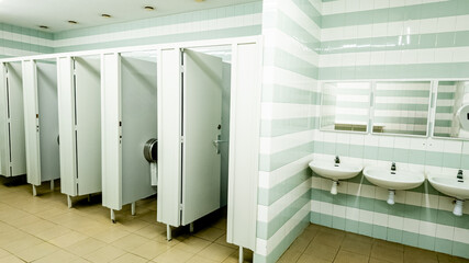 Clean public restroom interior with white partitioned doors and multiple sinks, representing hygiene and sanitation in communal spaces