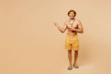 Full body young surprised man wear yellow shorts swimsuit hat relax rest near hotel pool point index finger aside on area isolated on plain beige background. Summer hot vacation sea sun tan concept.