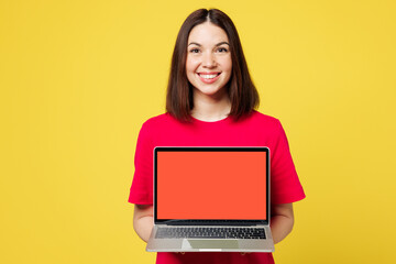 Naklejka premium Young smart IT woman wear pink t-shirt casual clothes hold use work on laptop pc computer with blank screen workspace area isolated on plain yellow orange background studio portrait Lifestyle concept