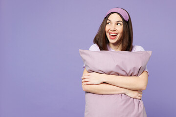 Fototapeta premium Young shocked fun surprised calm woman wear pyjamas jam sleep eye mask rest relax at home hold pillow look aside on area isolated on plain pastel purple background studio. Good mood night nap concept.