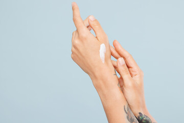 Close up cropped Caucasian female hand arm applying moisturizer cream from container isolated on pastel plain light blue color wall background studio. Skin care healthcare cosmetic procedures concept.