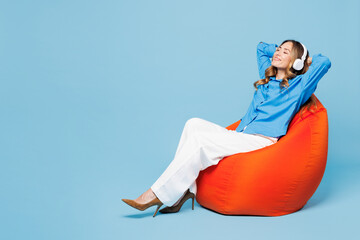 Full body young IT woman she wear shirt casual clothes sit in bag chair listen to music in...