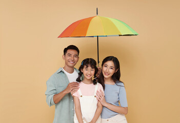 Happy asian family under big colorful umbrella isolated on nude color background. Family Protection and Life and health insurance concept.
