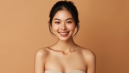Obraz premium A beautiful young Thai woman with an elegant updo hairstyle, smiling softly while standing against a light brown background.