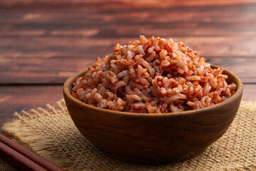 Cooked Thai Organic Red Jasmine Rice in wooden teak bowl.semi-milled rice.including fiber, offering a richer nutritional profile than traditional white rice.