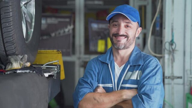 Worker in uniform holds wrench, car service. Mechanic looking up at camera at the repair garage.