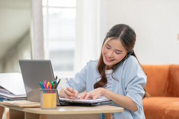Asian Woman Multitasking with Phone and Laptop While Taking Notes