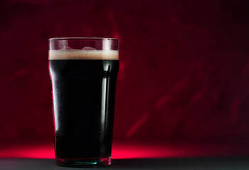 Dark craft beer on the table, red backlight. Copy space. Stout or porter
