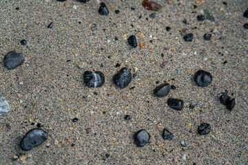 Round black rock pieces on the sand floor at nature beach.
