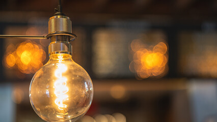 A classic designed tungsten lightbulb is glowing in orange warmlight shade with blurred background...
