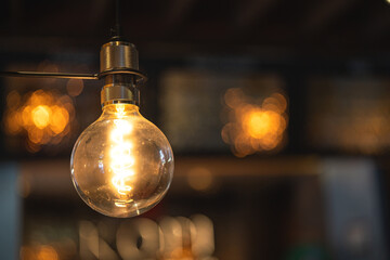 A classic designed tungsten lightbulb is glowing in orange warmlight shade with blurred background...