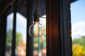 A classic designed tungsten lightbulb is glowing in orange warmlight shade with blurred background...