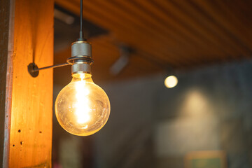 A classic designed tungsten lightbulb is glowing in orange warmlight shade with blurred background...