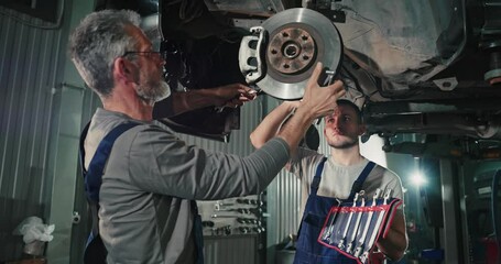At the auto service. Handsome young auto mechanics in uniform are smiling while repairing car