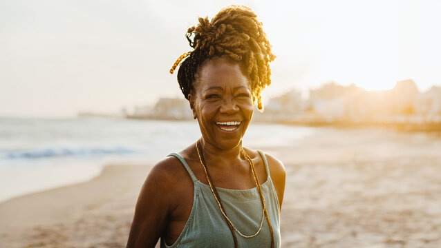 Happy senior African American woman with braids smiling at the beach during sunset