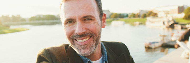 Close up, man makes selfie on mobile phone on the embankment of the river. Backlight