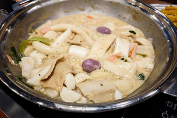 Delicious Korean Tteokbokki and Fish Cakes in Creamy Carbonara Sauce Served in a Stainless Steel Pan on a Wooden Table at a Cozy Restaurant