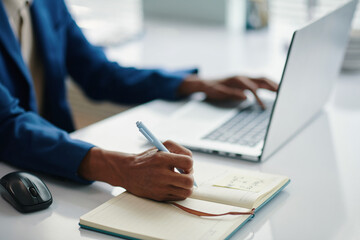 Hands of businessman working on laptop and taking notes in planner