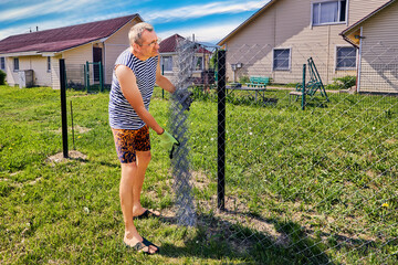 DIY chain link fence mesh installation, homeowner unwinds roll of steel mesh.