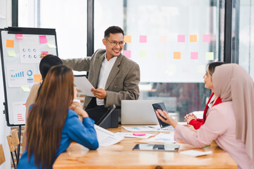 Diverse business team analyzing data and discussing strategies during an office meeting, using documents and a laptop.