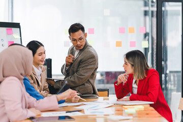 Confident businessman leading a meeting, engaging with colleagues while presenting data charts and graphs in a modern office.