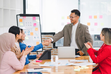 Business colleagues shaking hands and celebrating a successful presentation in a modern office.