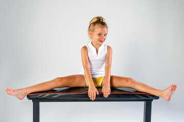 Confidently smiling young female gymnast or dancer doing splits on a practice bench
