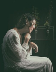 woman in white romantic dress sitting with a trunk full of plants and flowers on her legs VIII