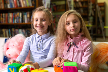 Two funny girls playing with alphabet blocks in the library