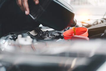 Close-up of a mechanic's hand pouring engine oil into a car's engine through a funnel during...