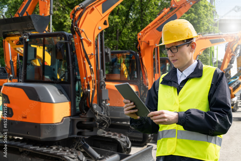 Aufkleber engineer in a helmet with a digital tablet stands next to construction excavators