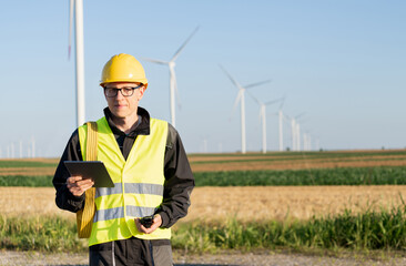 Engineer with digital tablet works on a field of wind turbines