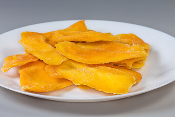 Dried mango slices on dish on gray background, side view