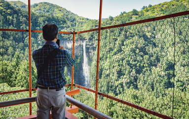  Back view with a tourist taking a picture with Nachi Waterfall located in Nachikatsuura, Wakayama,...