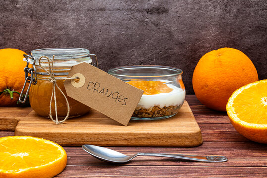 Glass jar full of muesli and yogurt with homemade orange jam, delicious snack with cheesecake and orange jam on wooden cutting board, detail with vintage cardboard tag