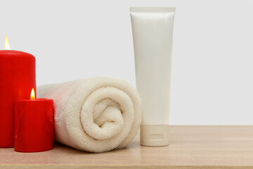 Two red candles, a white towel and a white container for cream.