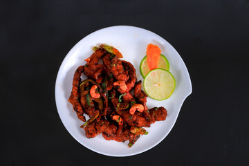 Schezwan Chicken or Dragon Chicken in black bowl at dark slate background.