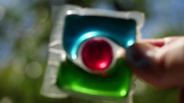 Laundry detergent pod. Men hand holds colorful water soluble sachet. Packs or liquitabs are water-soluble pouches containing highly concentrated laundry detergent, softener and other laundry products