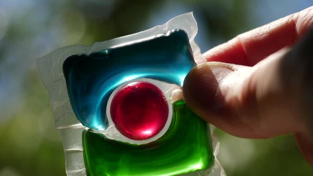 Laundry detergent pod. Men hand holds colorful water soluble sachet. Packs or liquitabs are water-soluble pouches containing highly concentrated laundry detergent, softener and other laundry products
